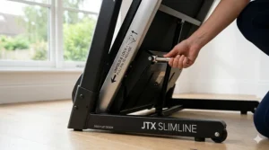 A side view of the JTX Slimline home treadmill being folded flat for easy storage under a bed or sofa.