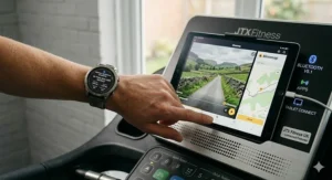 A tablet mounted on the JTX Sprint-9 console running the Kinomap app, displaying virtual UK running routes via Bluetooth connectivity.