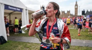 Marathon runner drinking a carbohydrate and protein recovery shake after finishing a race in Britain.